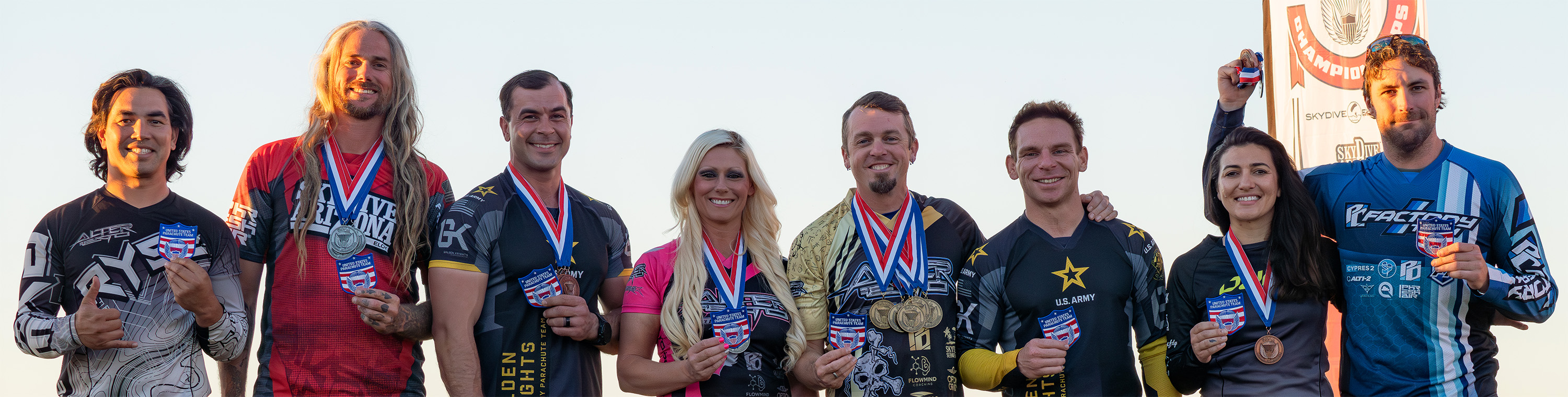 Eight members of the 2026-2027 Canopy Piloting Team standing side-by-side, holding U.S. Parachute Team patches. Photographed by Leah Levy.